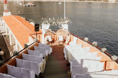 Un couple en tenue élégante regarde la mer au coucher du soleil, avec un bateau visible à l'horizon.