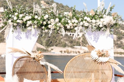 Un couple en tenue élégante regarde la mer au coucher du soleil, avec un bateau visible à l'horizon.