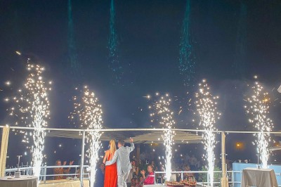 Un cocktail orange garni d'un demi-fruit de la passion, tenu par une main sur une table dressée en extérieur.