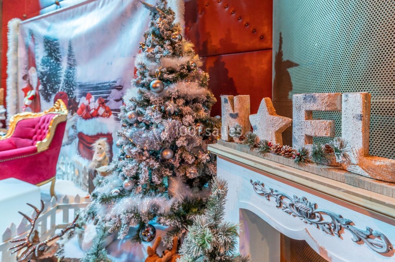 Sapin de Noël décoré avec guirlandes et boules, cheminée ornée et lettres ’Noël’ en bois dans un décor festif.
