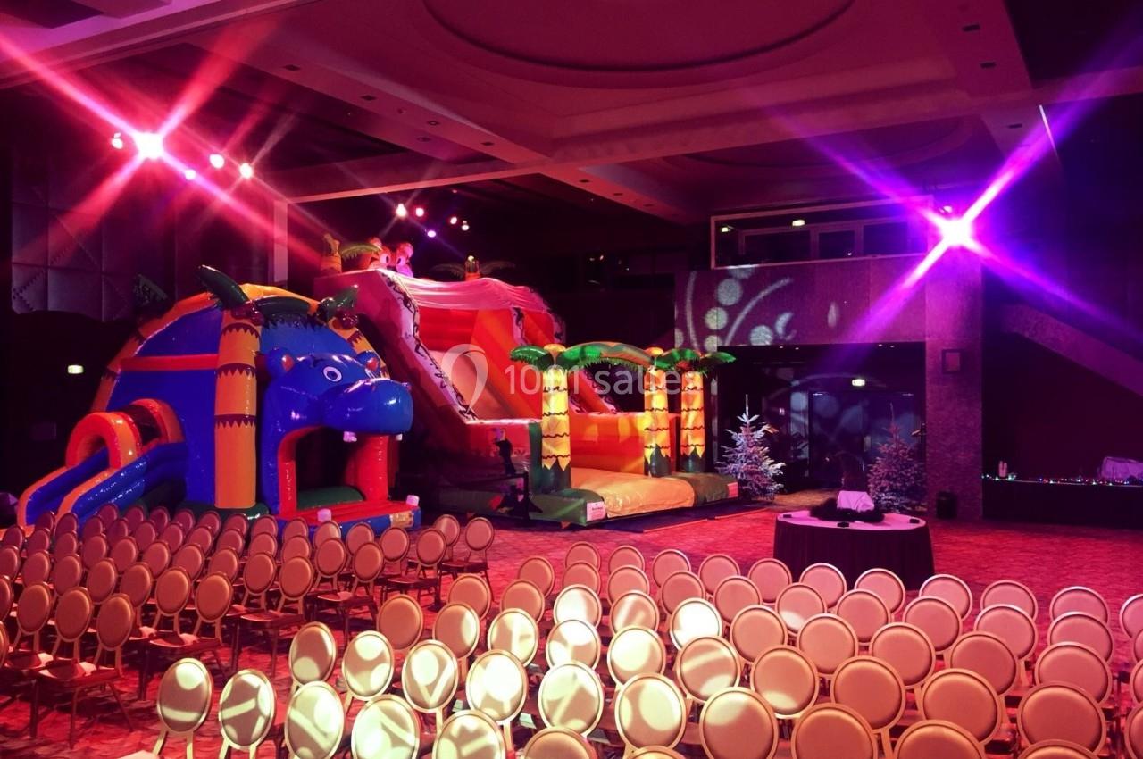 Deux structures gonflables colorées dans une salle de réception éclairée, avec des rangées de chaises vides au premier plan.