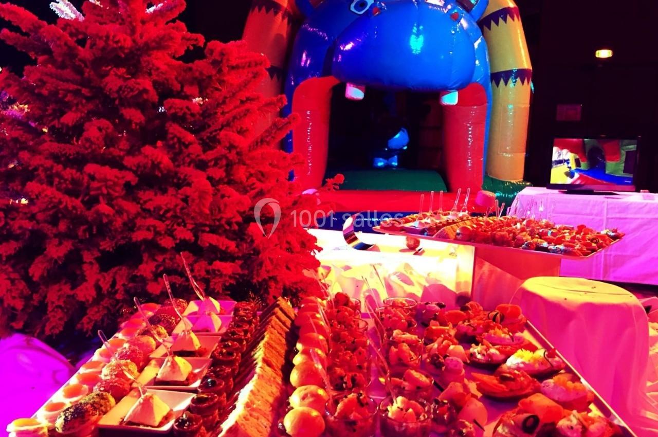 Buffet de petits fours variés devant un sapin rouge et une structure gonflable colorée en arrière-plan.