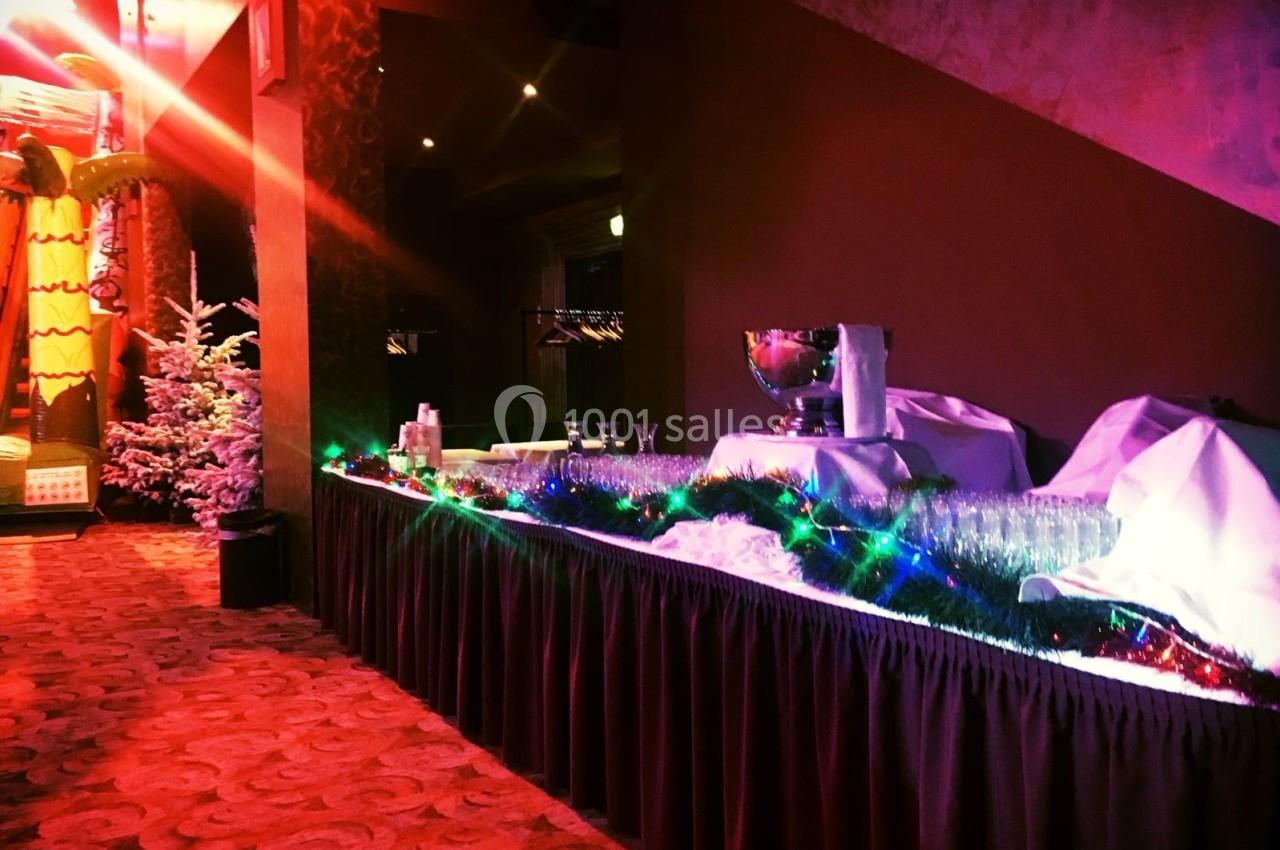Table décorée avec des guirlandes lumineuses, contenant des verres et un seau à champagne, dans un espace intérieur festif.