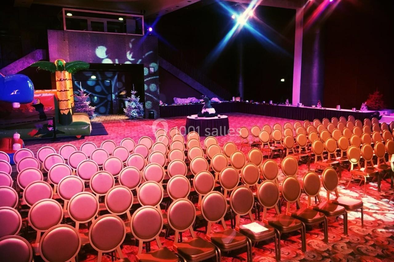 Salle de conférence avec des rangées de chaises alignées, une table centrale et une décoration lumineuse colorée.