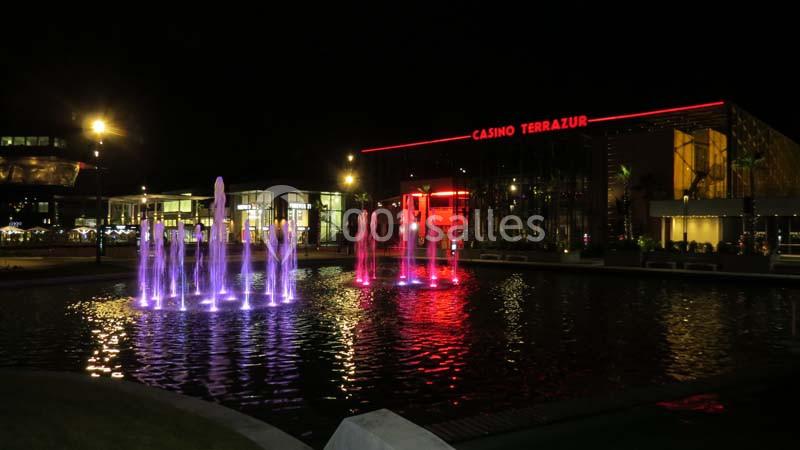 Fontaines illuminées en rose et violet devant un bâtiment moderne avec l'enseigne ’Casino Terrazur’ éclairée en rouge.