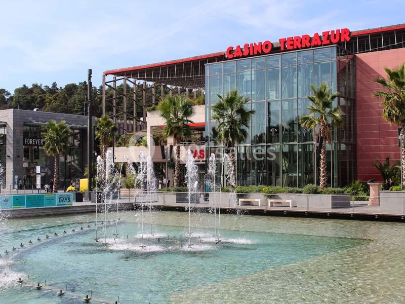 Façade moderne du Casino Terrazur avec une fontaine au premier plan et des palmiers bordant l'entrée.