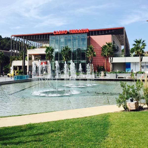 Façade du casino Terrazur avec une fontaine entourée de palmiers et d'espaces verts au premier plan.