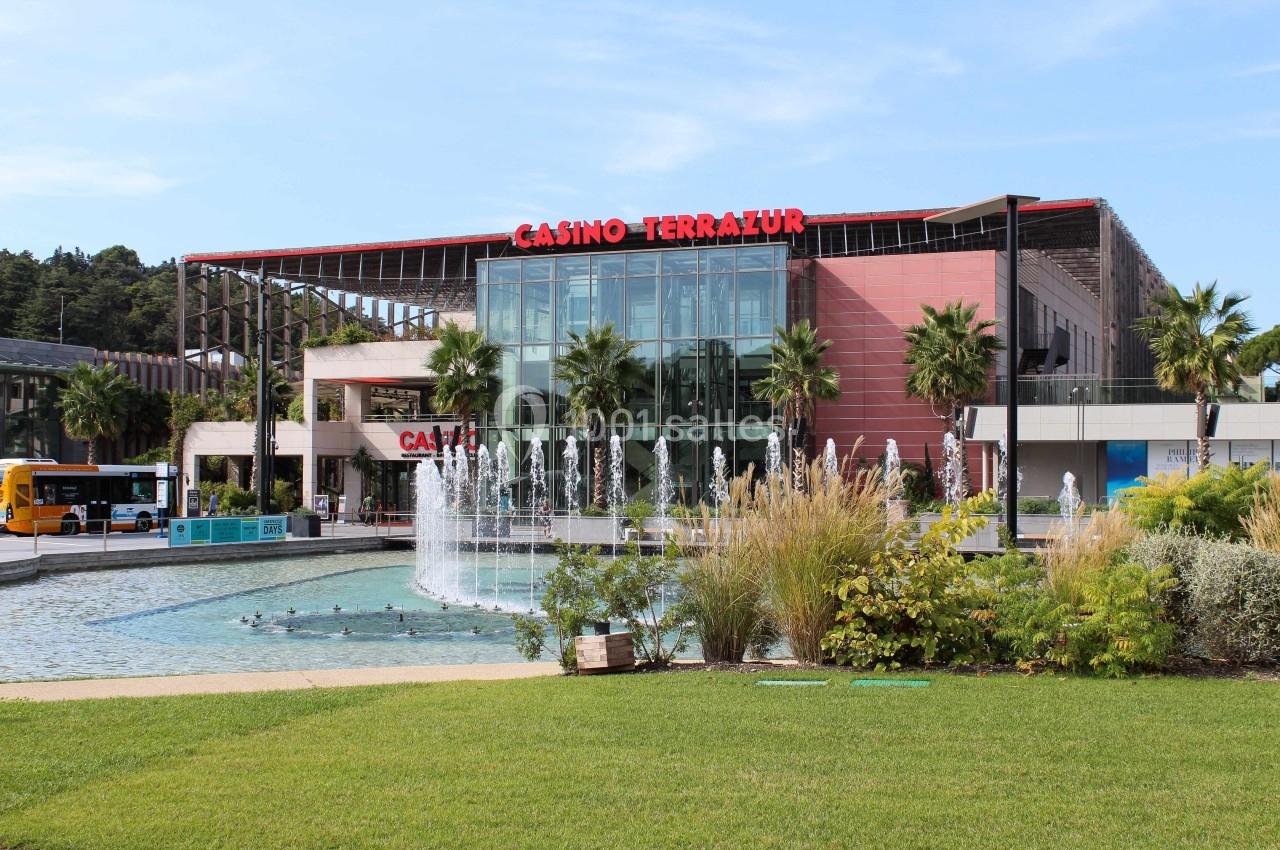 Façade du Casino Terrazur avec fontaine, palmiers et végétation au premier plan, sous un ciel dégagé.