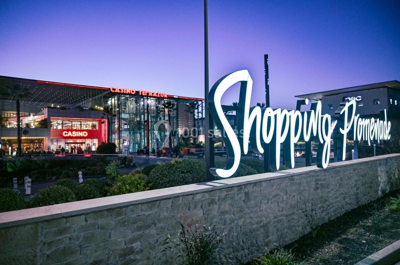 Enseigne lumineuse ’Shopping Promenade’ devant un centre commercial avec casino, de nuit.
