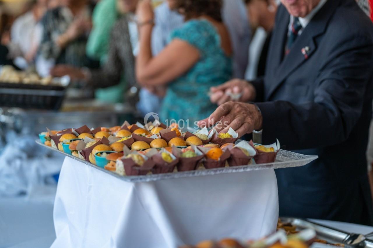 Plateau de petits gâteaux et amuse-bouches sur une table lors d'un événement avec des invités en arrière-plan.