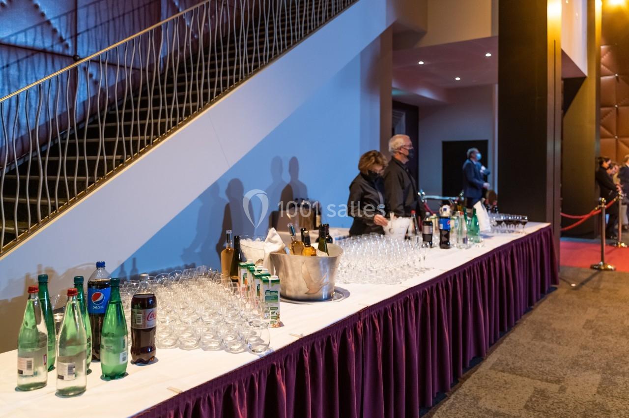 Table avec boissons variées, verres et seau à glace, située dans un espace intérieur avec un escalier en arrière-plan.