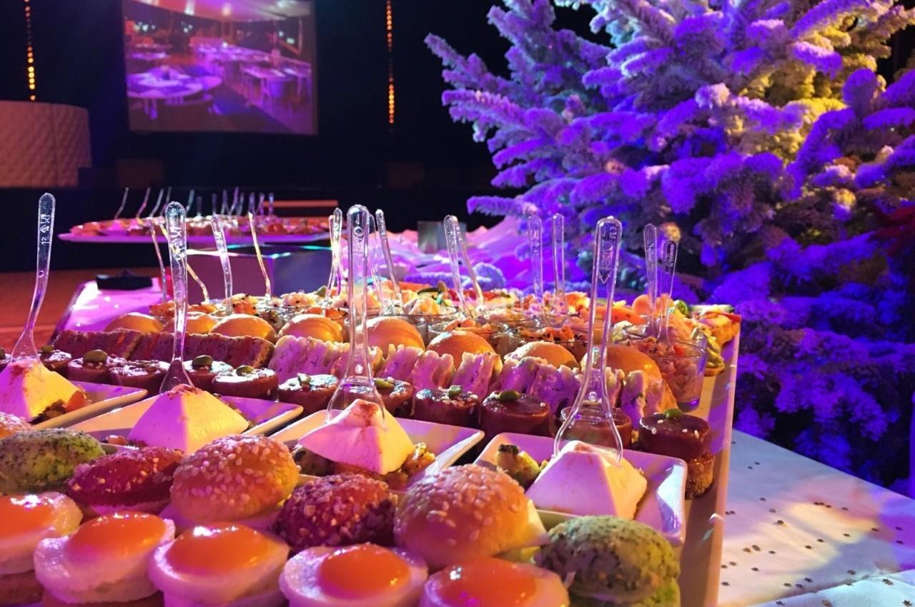 Plateau de bouchées salées et sucrées disposées sur une table décorée, avec un sapin enneigé en arrière-plan.