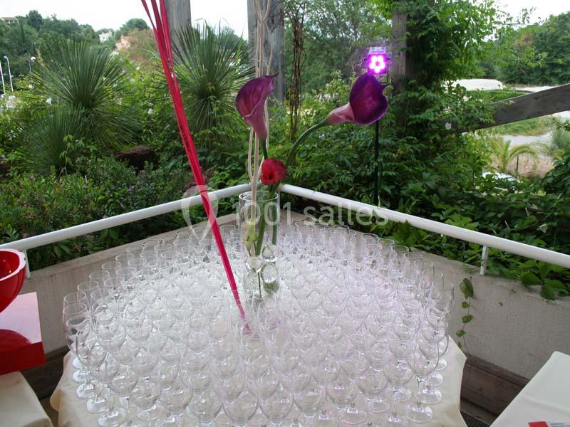 Centre de table avec des verres à pied disposés en cercle autour d'un vase contenant des fleurs violettes et rouges.