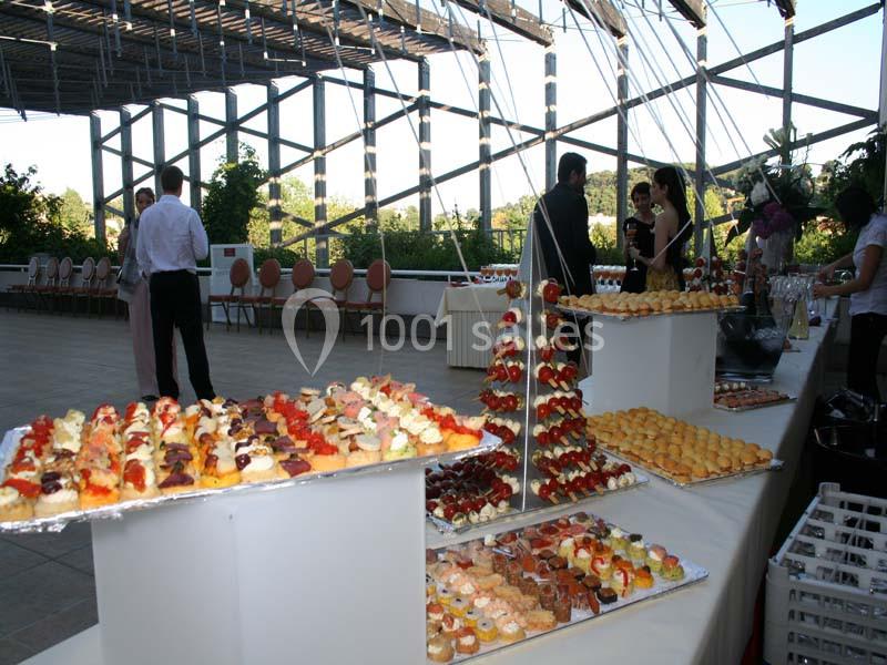 Buffet de pâtisseries variées disposées sur des tables dans une salle lumineuse avec des invités en arrière-plan.