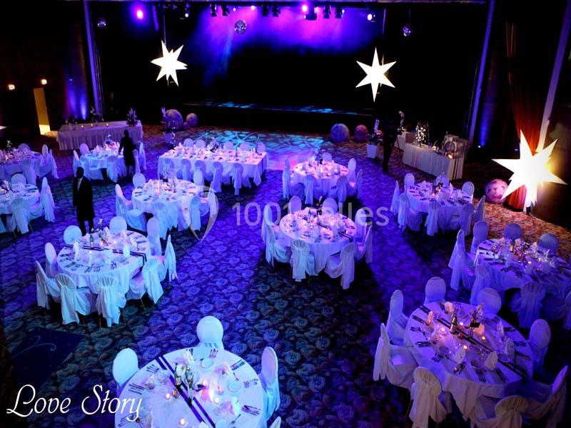 Salle de réception décorée avec des tables rondes dressées, éclairage violet et étoiles lumineuses suspendues.