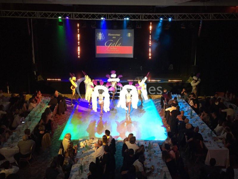 Des danseuses en costume de cabaret se produisent sur une scène éclairée, entourée de tables avec des spectateurs.
