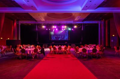 Salle lumineuse avec tables et chaises modernes, sol en moquette, cloison en bois et tapis rouge au centre.