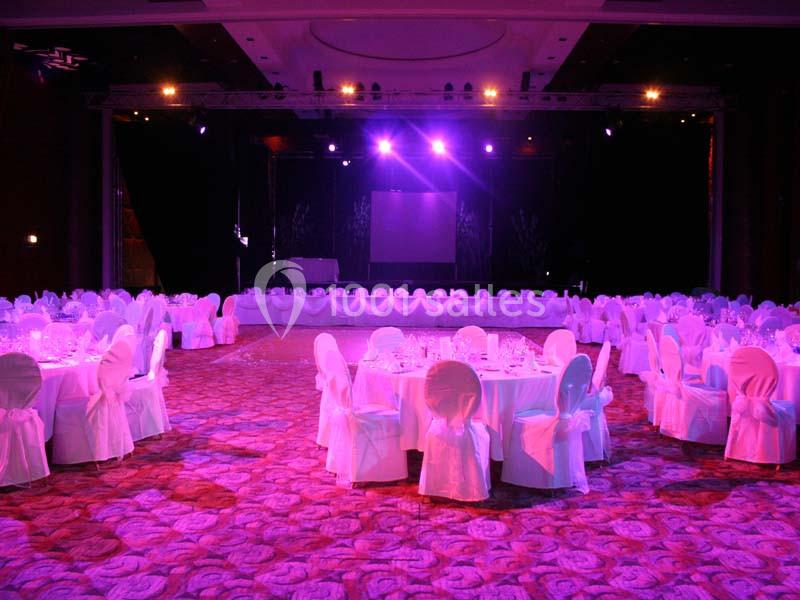 Salle de réception éclairée en violet, tables rondes dressées avec nappes blanches et chaises assorties.