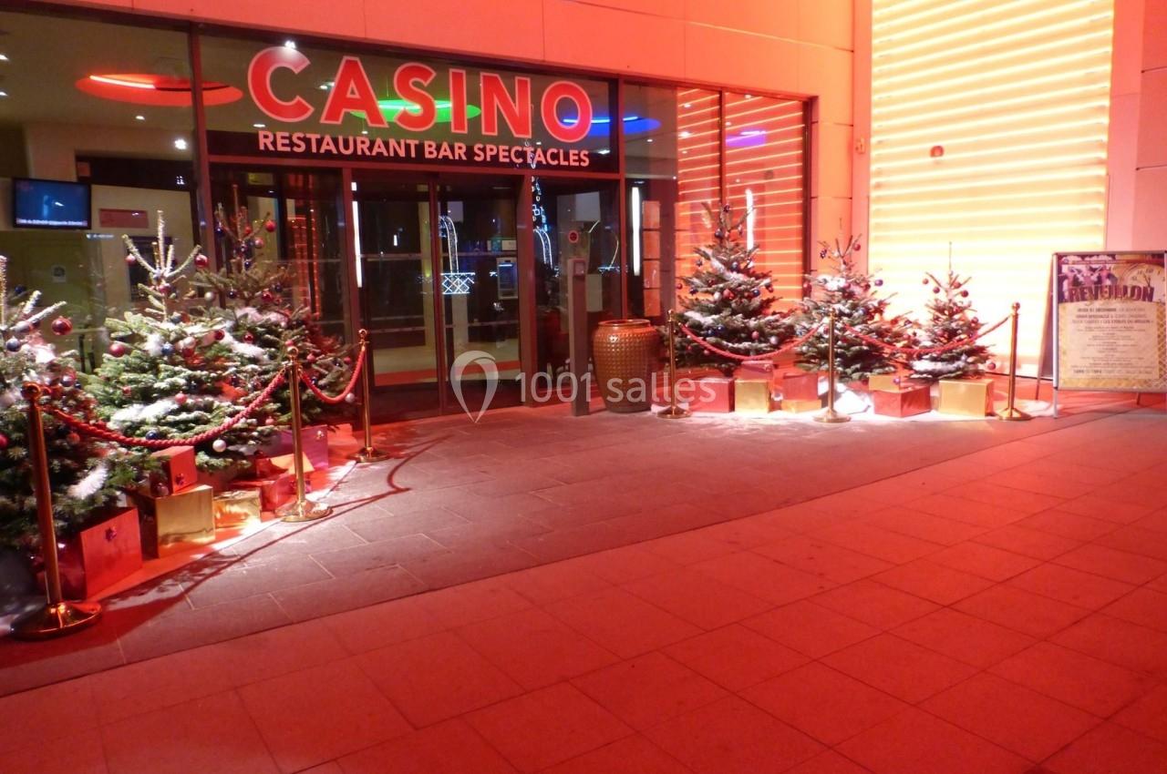 Entrée d'un casino décorée pour Noël avec des sapins illuminés et des cadeaux disposés devant la façade.
