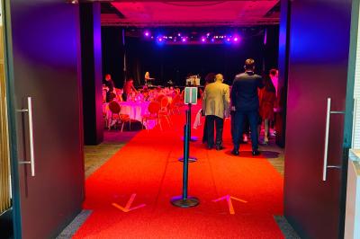 Salle lumineuse avec tables et chaises modernes, sol en moquette, cloison en bois et tapis rouge au centre.
