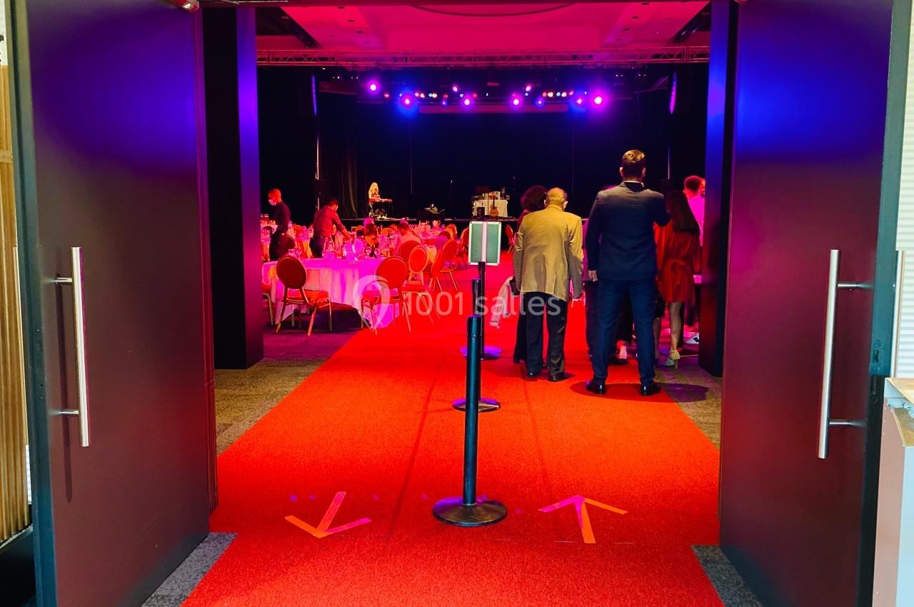 Entrée d'une salle de réception avec tapis rouge, tables dressées et éclairage violet en arrière-plan.