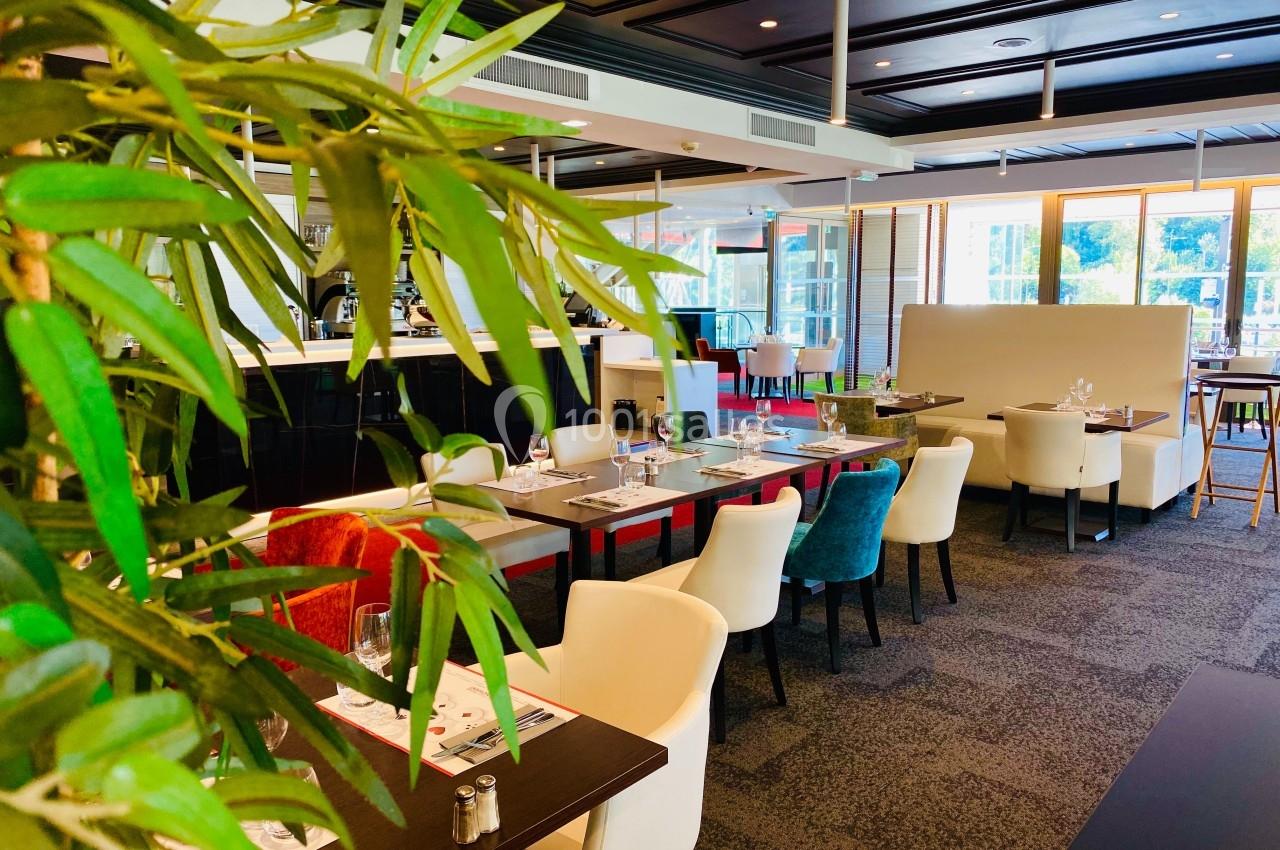 Salle de restaurant lumineuse avec tables dressées, chaises colorées et plantes décoratives au premier plan.