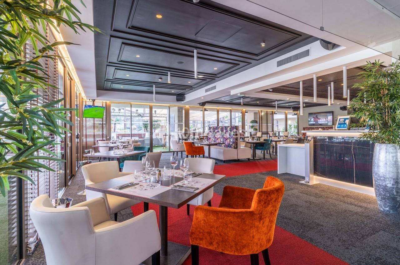 Salle de restaurant moderne avec tables dressées, chaises colorées et décoration végétale.