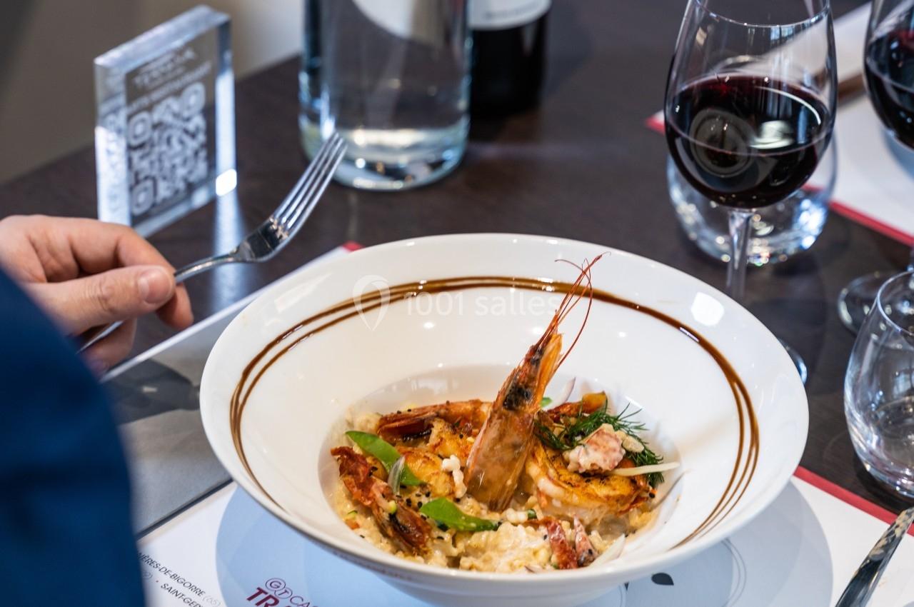 Assiette de risotto aux fruits de mer avec une crevette entière, servie sur une table avec des verres de vin rouge.