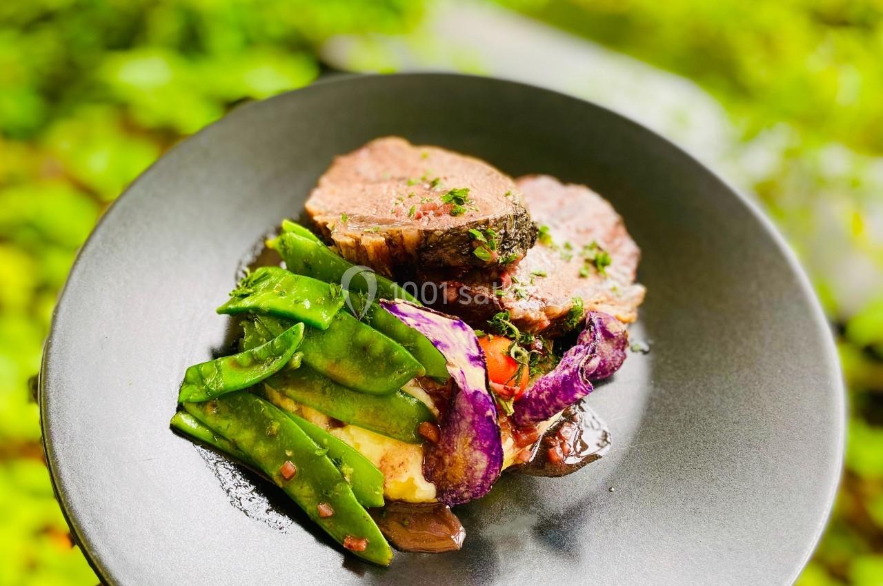 Assiette contenant de la viande, des pois mange-tout, des chips de légumes violets et une purée, présentée sur un fond…