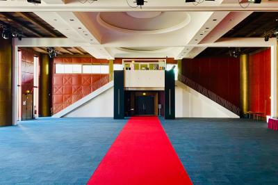 Salle lumineuse avec tables et chaises modernes, sol en moquette, cloison en bois et tapis rouge au centre.