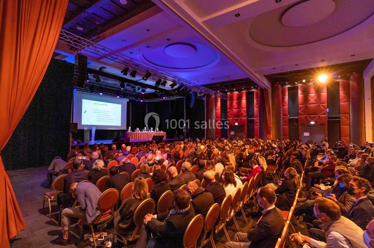 Salle de conférence remplie de participants assis, regardant une présentation projetée sur un écran.