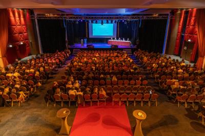 Salle lumineuse avec tables et chaises modernes, sol en moquette, cloison en bois et tapis rouge au centre.