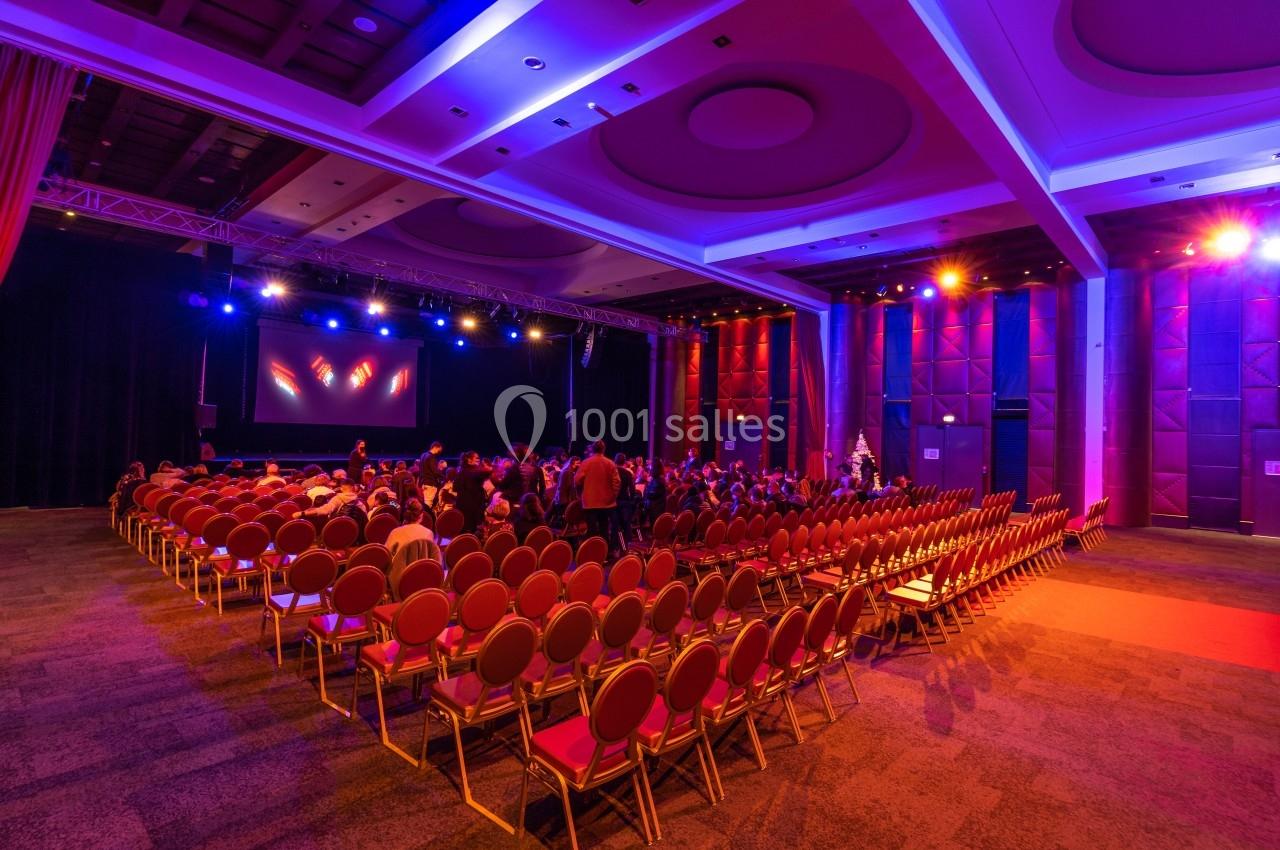 Salle de conférence avec des rangées de chaises rouges, un écran de projection et un éclairage coloré.