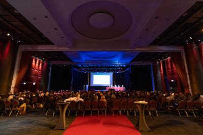 Salle lumineuse avec tables et chaises modernes, sol en moquette, cloison en bois et tapis rouge au centre.