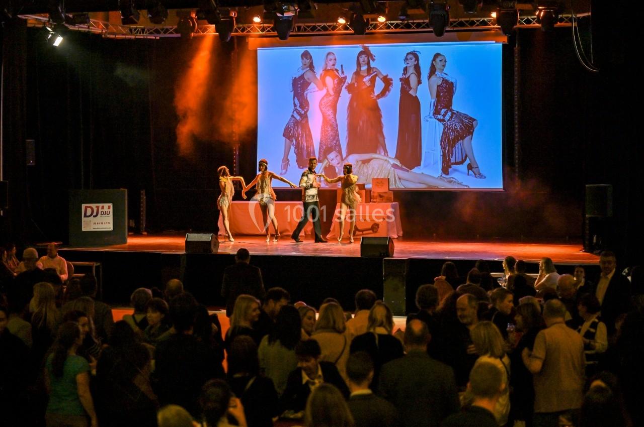Des danseurs sur scène exécutent une chorégraphie devant un public, avec une image projetée en arrière-plan.