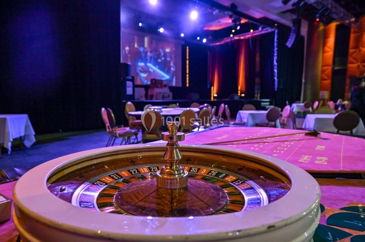 Roulette de casino en gros plan dans une salle éclairée avec des tables de jeu et un écran en arrière-plan.