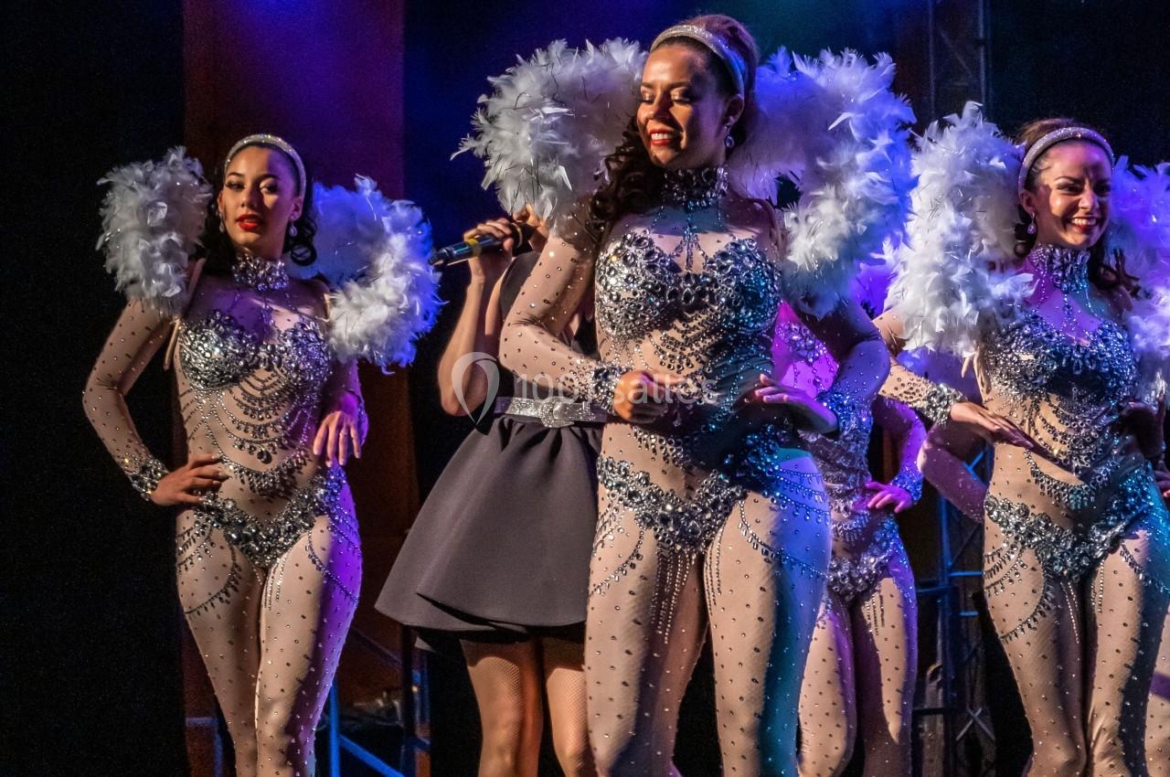 Des danseuses en costumes scintillants avec des plumes blanches se produisent sur une scène éclairée.