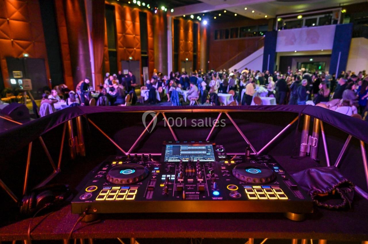 Vue d'une table de mixage de DJ en premier plan, avec une salle remplie de convives en arrière-plan.
