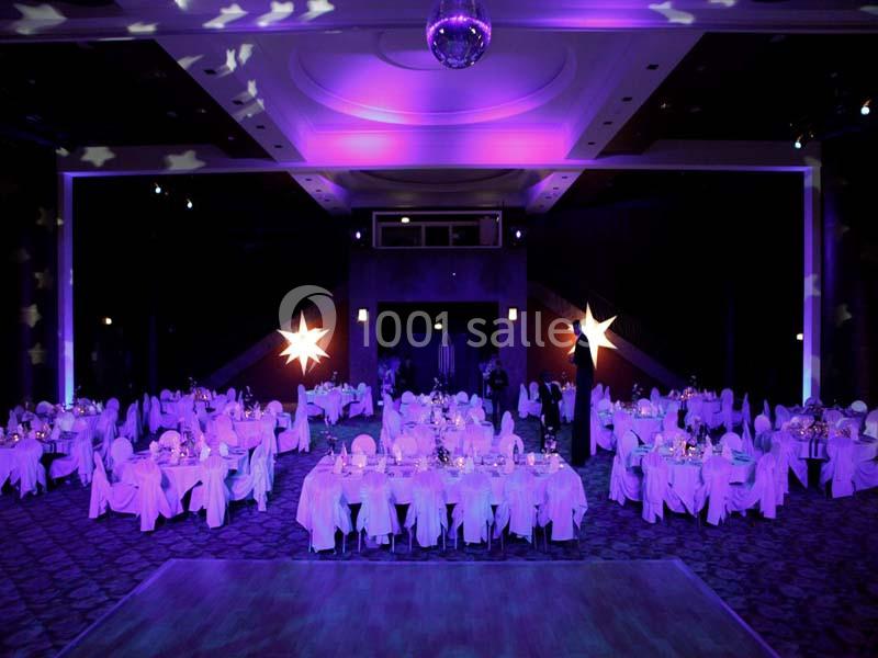 Salle de réception décorée avec des tables rondes, nappes blanches et éclairage violet créant une ambiance festive.