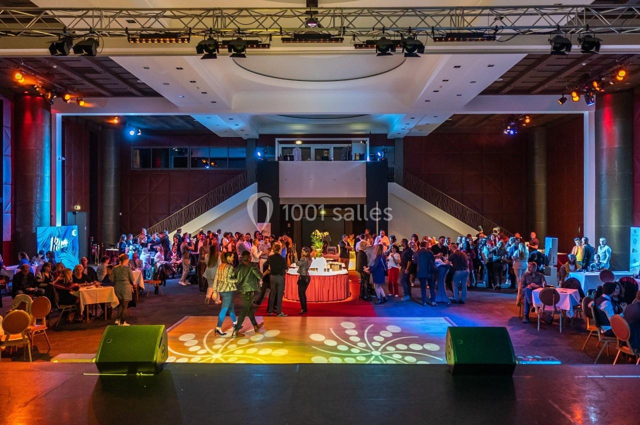 Salle de réception avec des invités debout et assis autour de tables, éclairée par des lumières colorées.