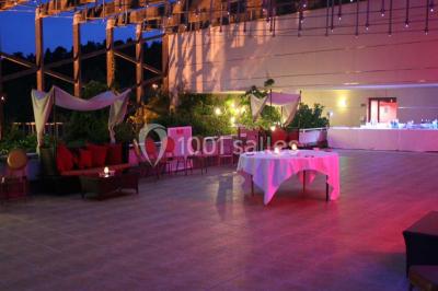 Salle lumineuse avec tables et chaises modernes, sol en moquette, cloison en bois et tapis rouge au centre.