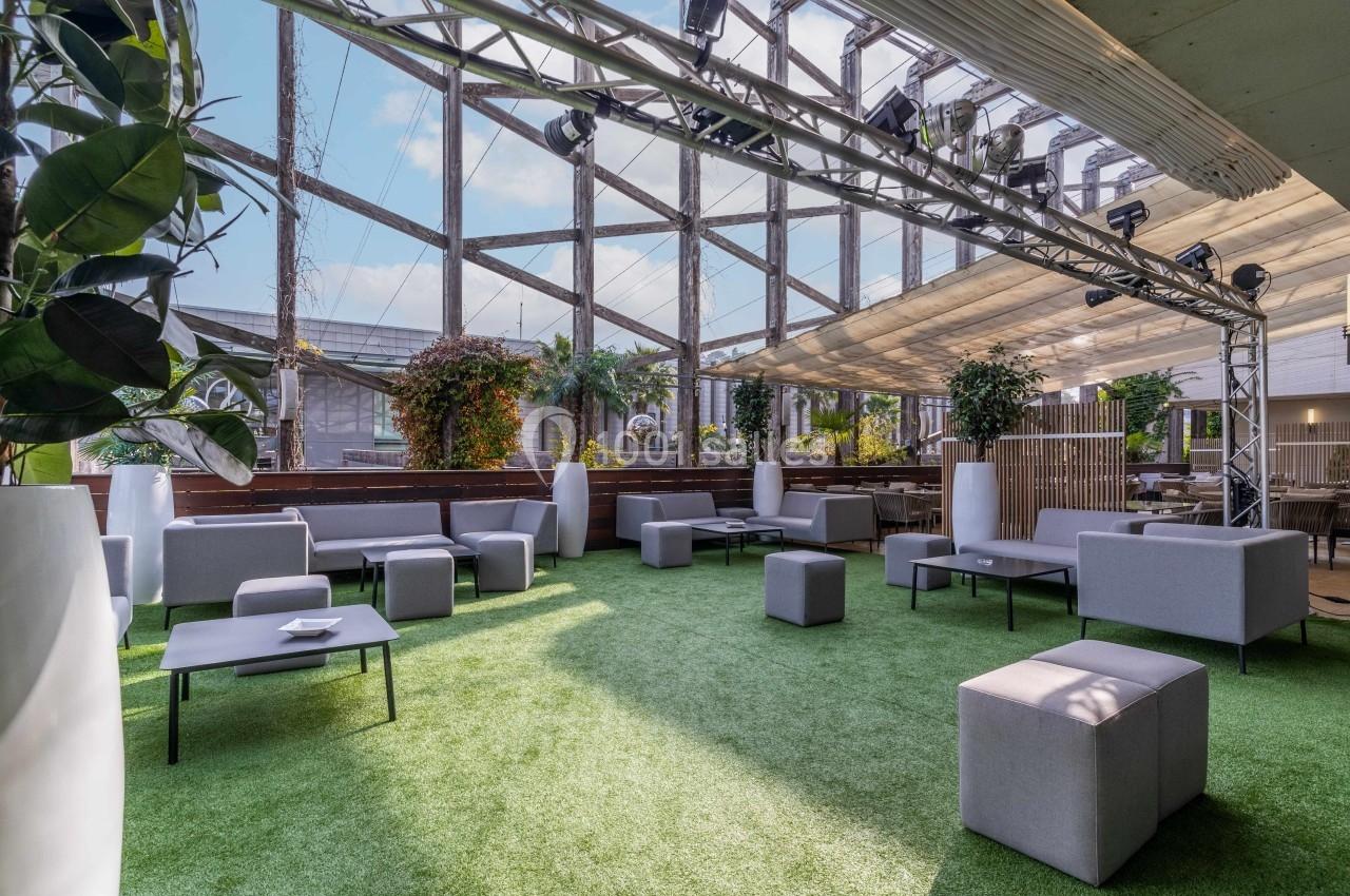 Espace extérieur aménagé avec des sièges modernes, du gazon artificiel et des plantes sous une structure lumineuse.