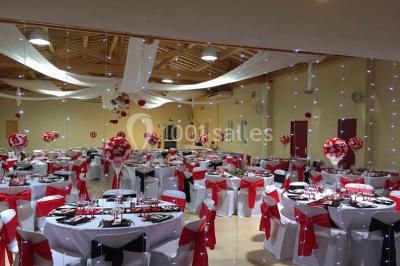 Terrasse extérieure éclairée la nuit, avec des tables et chaises en fer forgé entourées de fleurs colorées.