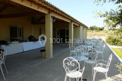 Terrasse extérieure éclairée la nuit, avec des tables et chaises en fer forgé entourées de fleurs colorées.