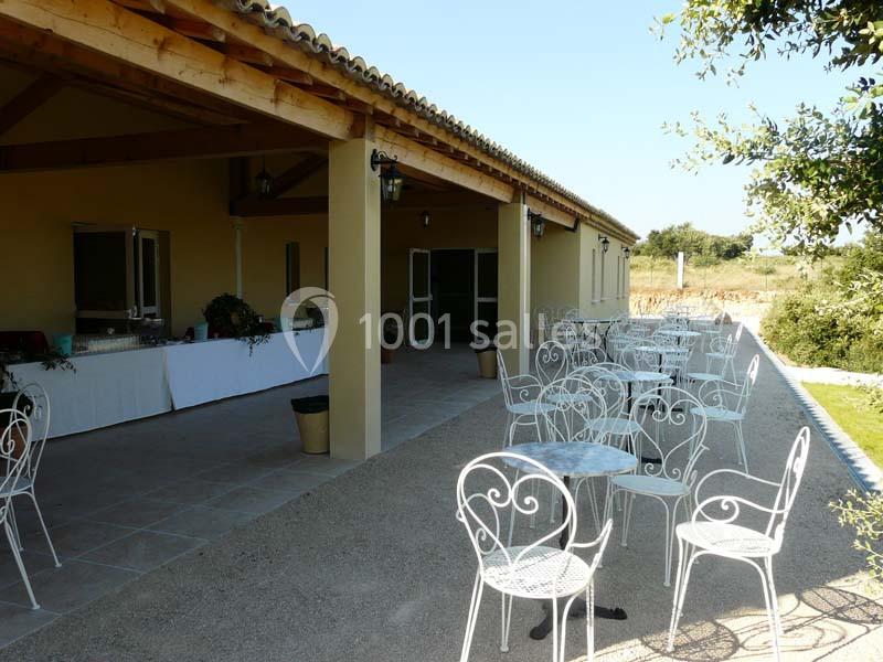 Terrasse avec tables et chaises en fer forgé, adossée à un bâtiment avec toit en tuiles et vue sur un espace naturel.