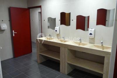 Terrasse extérieure éclairée la nuit, avec des tables et chaises en fer forgé entourées de fleurs colorées.