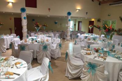 Terrasse extérieure éclairée la nuit, avec des tables et chaises en fer forgé entourées de fleurs colorées.