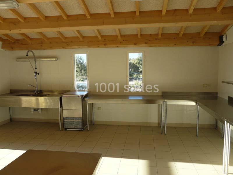 Cuisine collective lumineuse avec plan de travail en inox, évier, et plafond en bois sous une toiture inclinée.