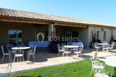 Terrasse extérieure éclairée la nuit, avec des tables et chaises en fer forgé entourées de fleurs colorées.