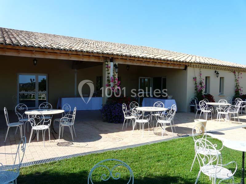 Terrasse avec tables et chaises en fer forgé, devant un bâtiment beige avec toit en tuiles et décorations florales.